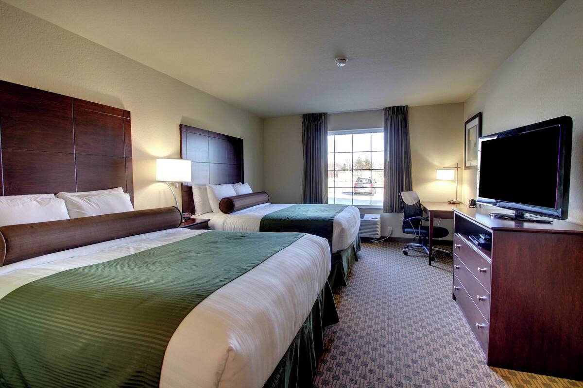 A hotel room with two beds, a desk, a chair, a television, and a window with curtains.
