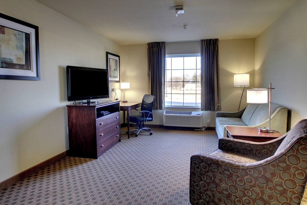 A hotel room with a desk, chair, television, and a sofa.