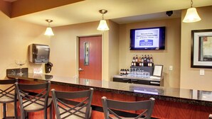 A bar area with a counter, bar stools, a television screen displaying a welcome message, and a wall-mounted dispenser. - Cobblestone Hotel & Suites - Newton (Newton)