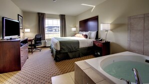 A hotel room with a bed, a desk with a computer, a chair, a desk lamp, a TV, and a bathtub. - Cobblestone Hotel & Suites - Newton (Newton)