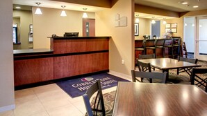 A hotel lobby with a reception desk, a seating area with tables and chairs, and a carpet with the hotel's name. - Cobblestone Hotel & Suites - Newton (Newton)