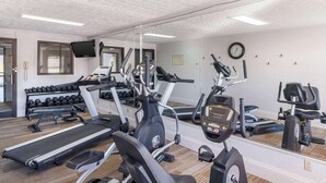Un gimnasio con cintas de correr, máquinas elípticas y un banco con mancuernas.