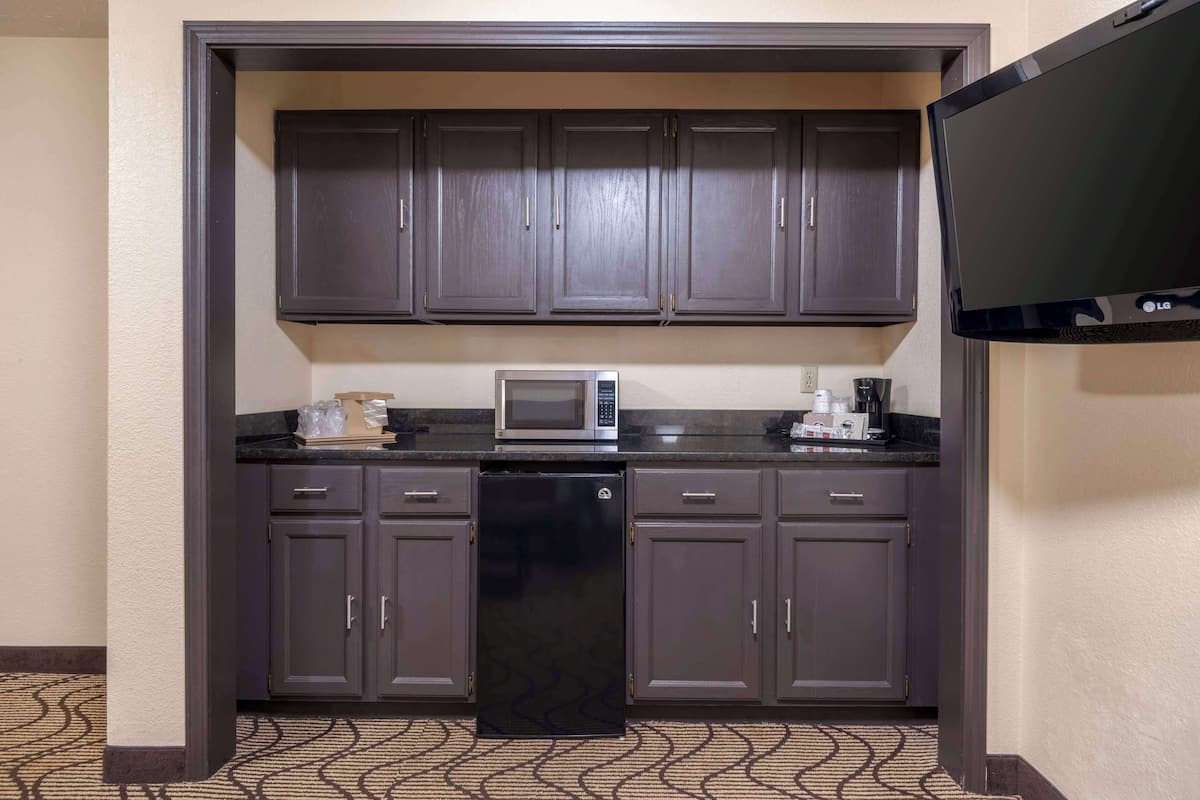 Una kitchenette compacta con armarios oscuros, un microondas, una cafetera y un televisor de pantalla plana.