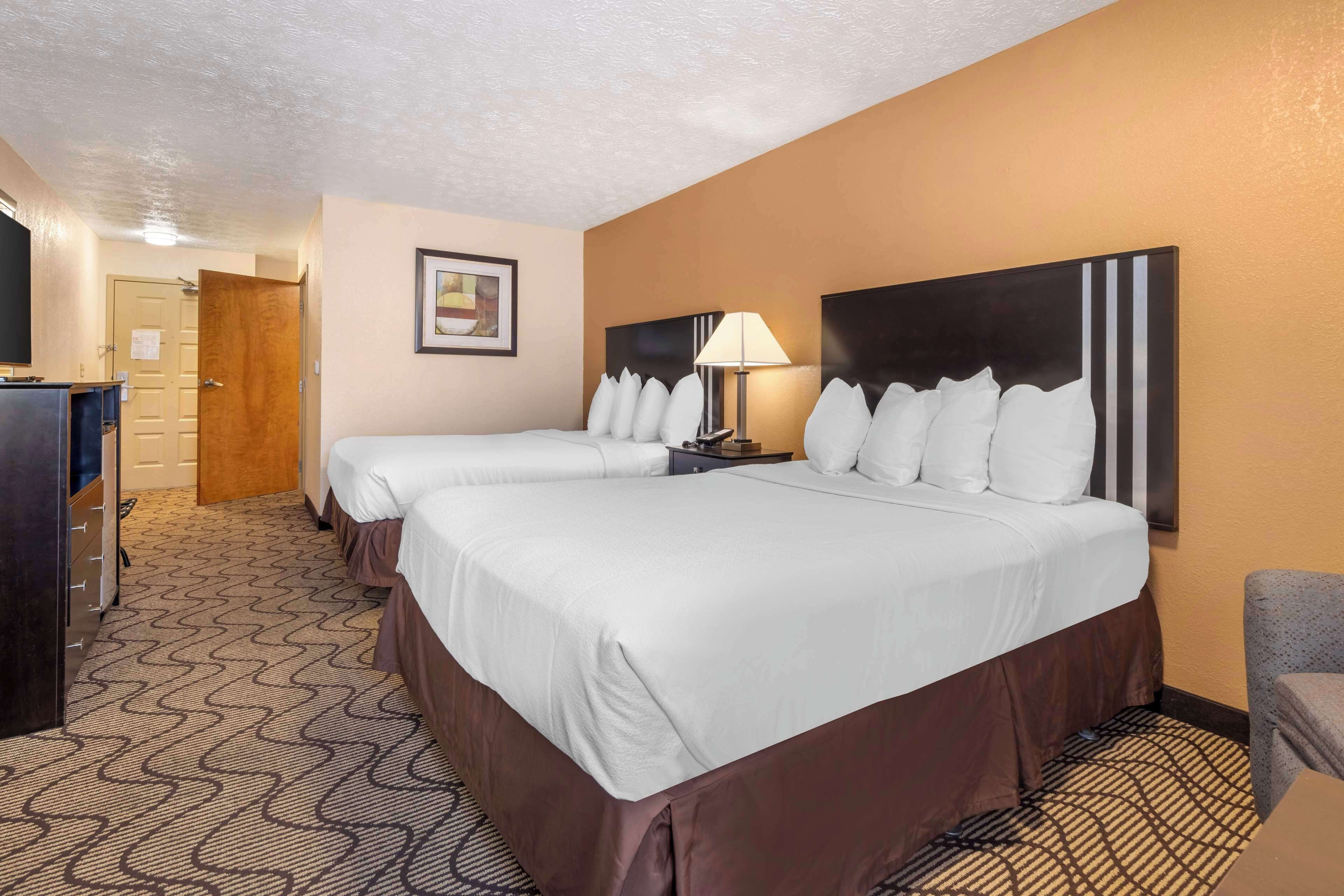 A hotel room with two beds, a desk, a lamp, and a chair.