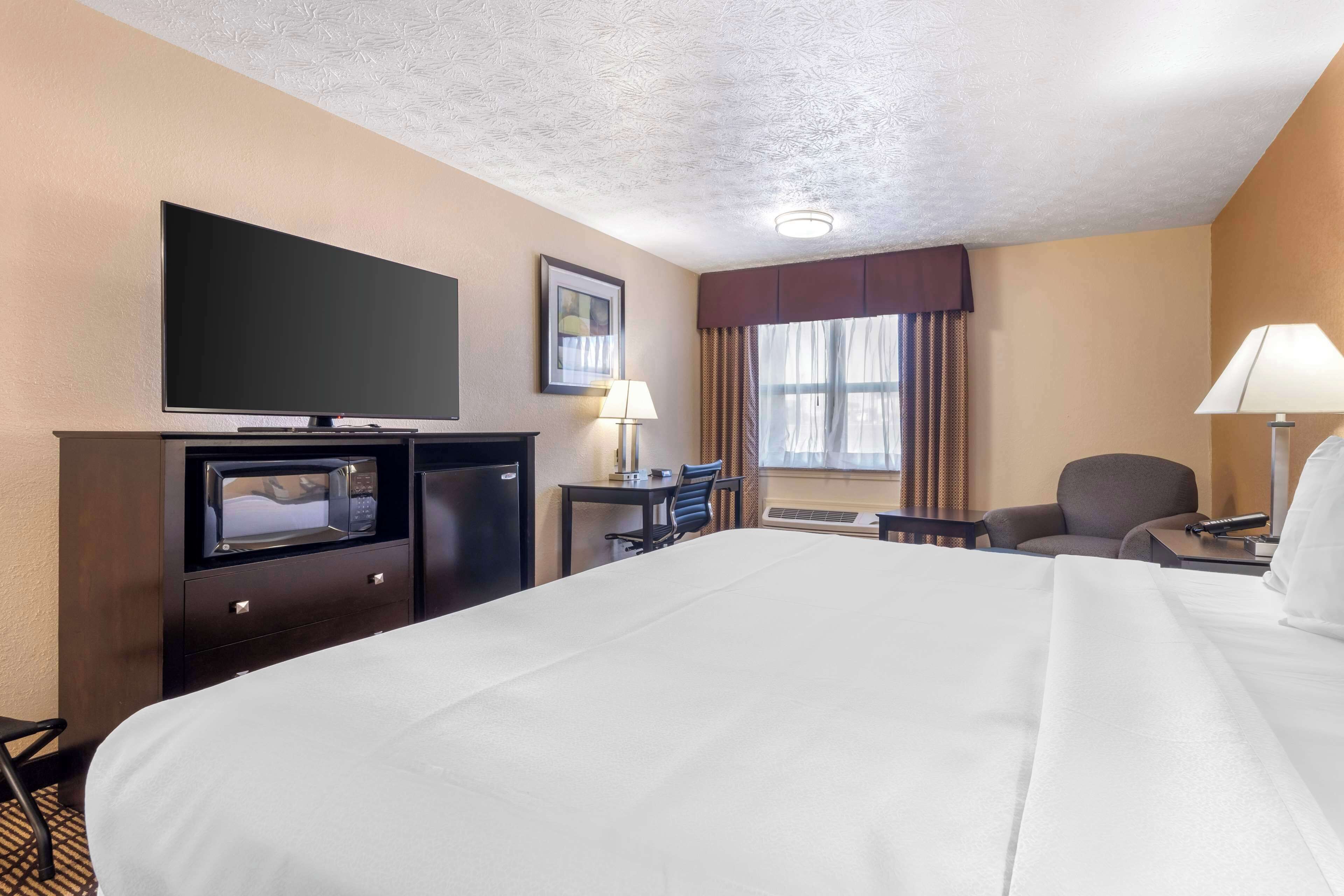 Una habitación de hotel con una cama grande, un televisor de pantalla plana, un escritorio con lámpara y una silla.