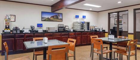 A hotel lobby with a reception desk, a coffee station, and a seating area with tables and chairs.