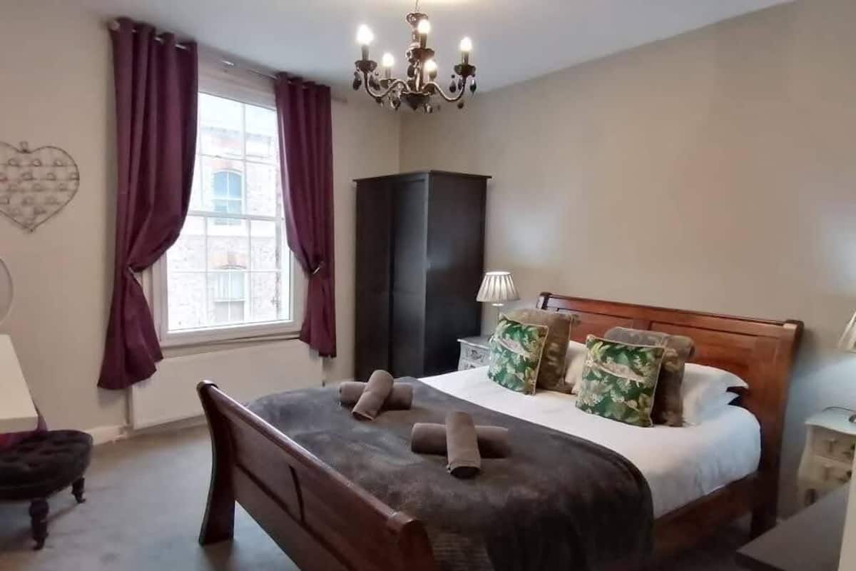 Une chambre à coucher avec un lit en bois, une table de chevet, une lampe, une armoire et une fenêtre avec des rideaux.