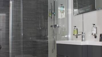 Un baño moderno con ducha de vidrio, un lavamanos blanco y muebles oscuros.