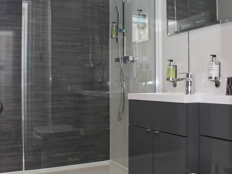 Un baño moderno con ducha de vidrio, un lavamanos blanco y muebles oscuros.