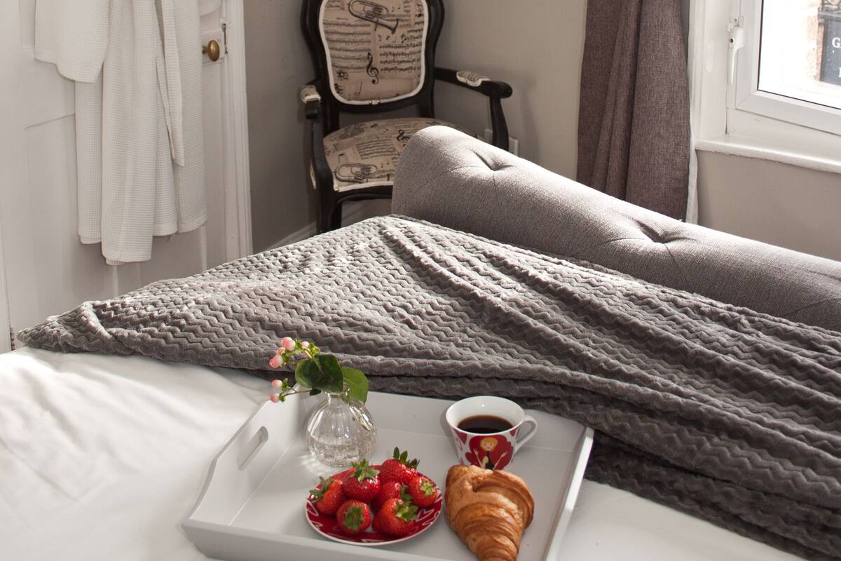 Un lit bien fait, avec un plateau contenant des fraises, un croissant et une tasse de café.