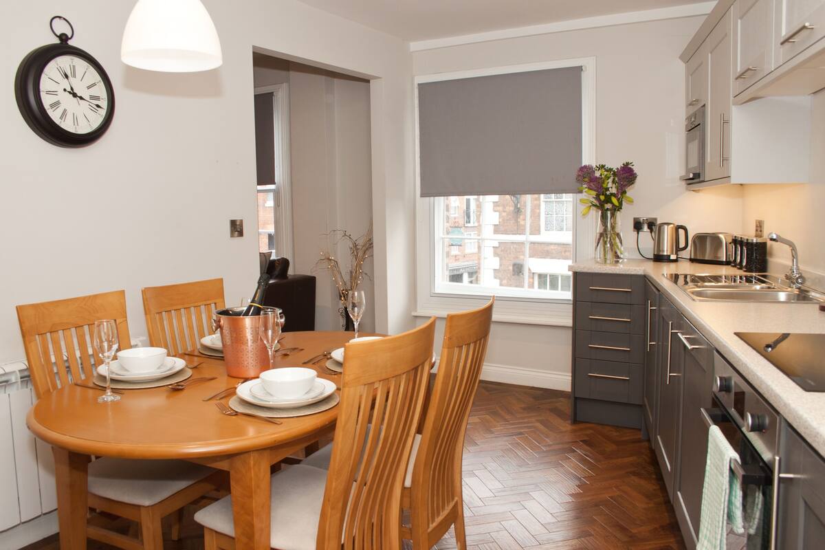 Une cuisine moderne avec un coin repas, comprenant une table en bois, des chaises, une horloge et une fenêtre donnant sur un beau paysage.