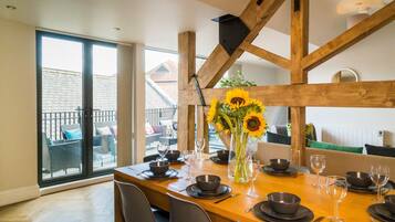 A dining area with a wooden table set for six, large windows, and a view of the outside balcony.