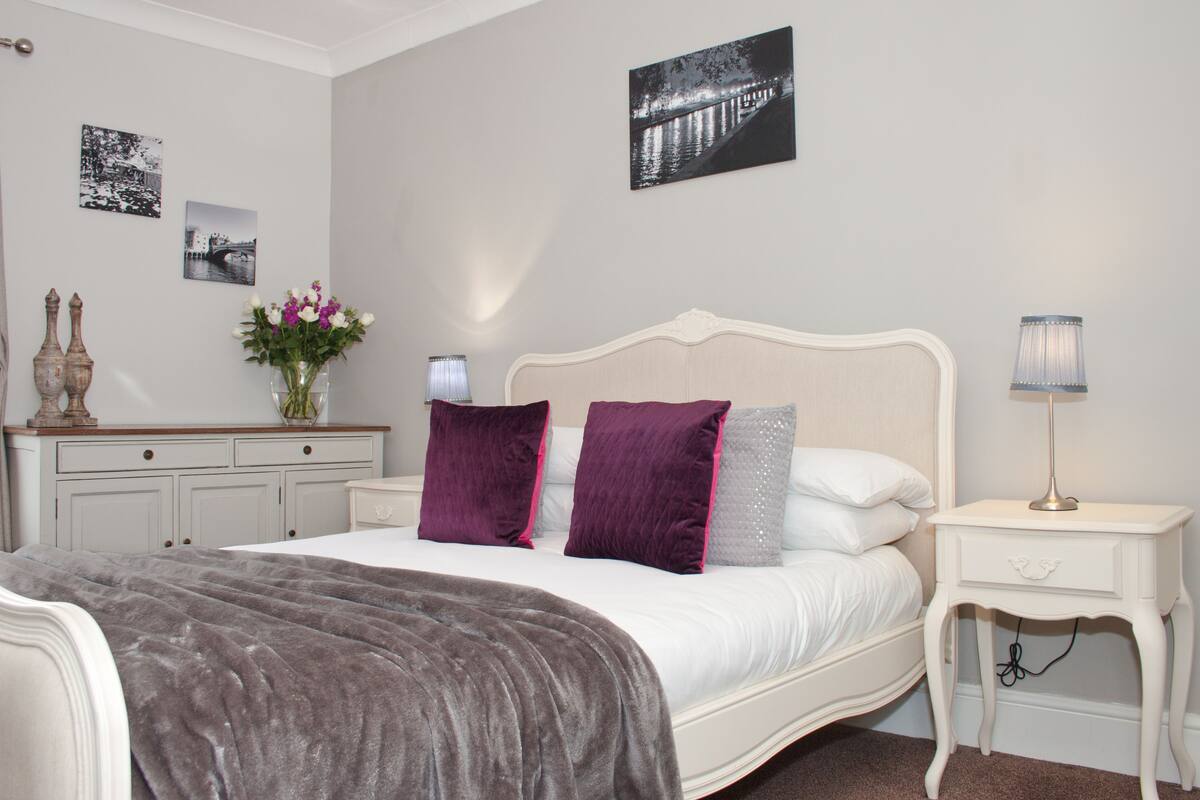 Une chambre à coucher comprenant un lit, des tables de chevet, une commode, une lampe et des œuvres d’art murales.