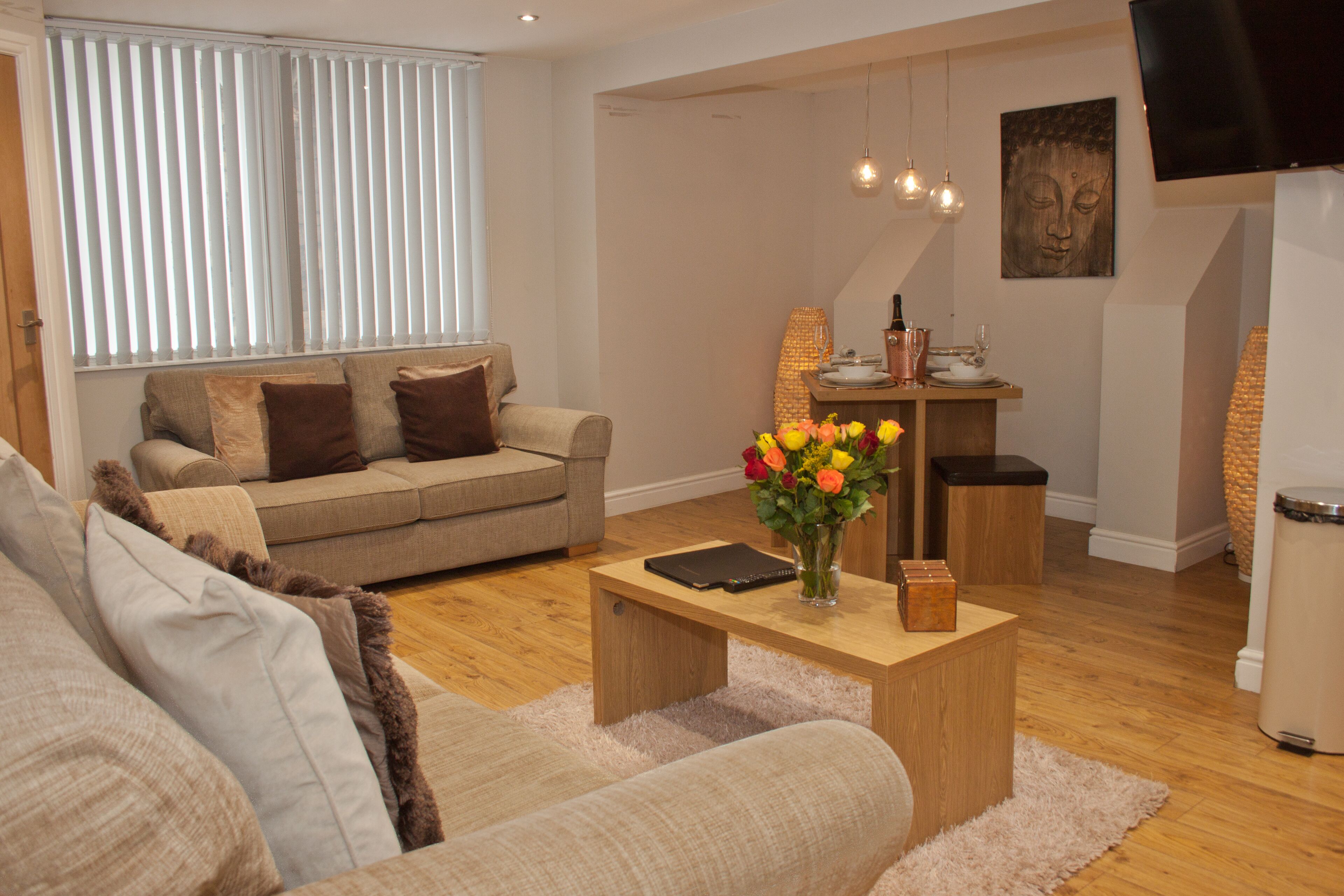A modern living room with a sofa, coffee table, and a small dining area with a lamp and a Buddha painting.