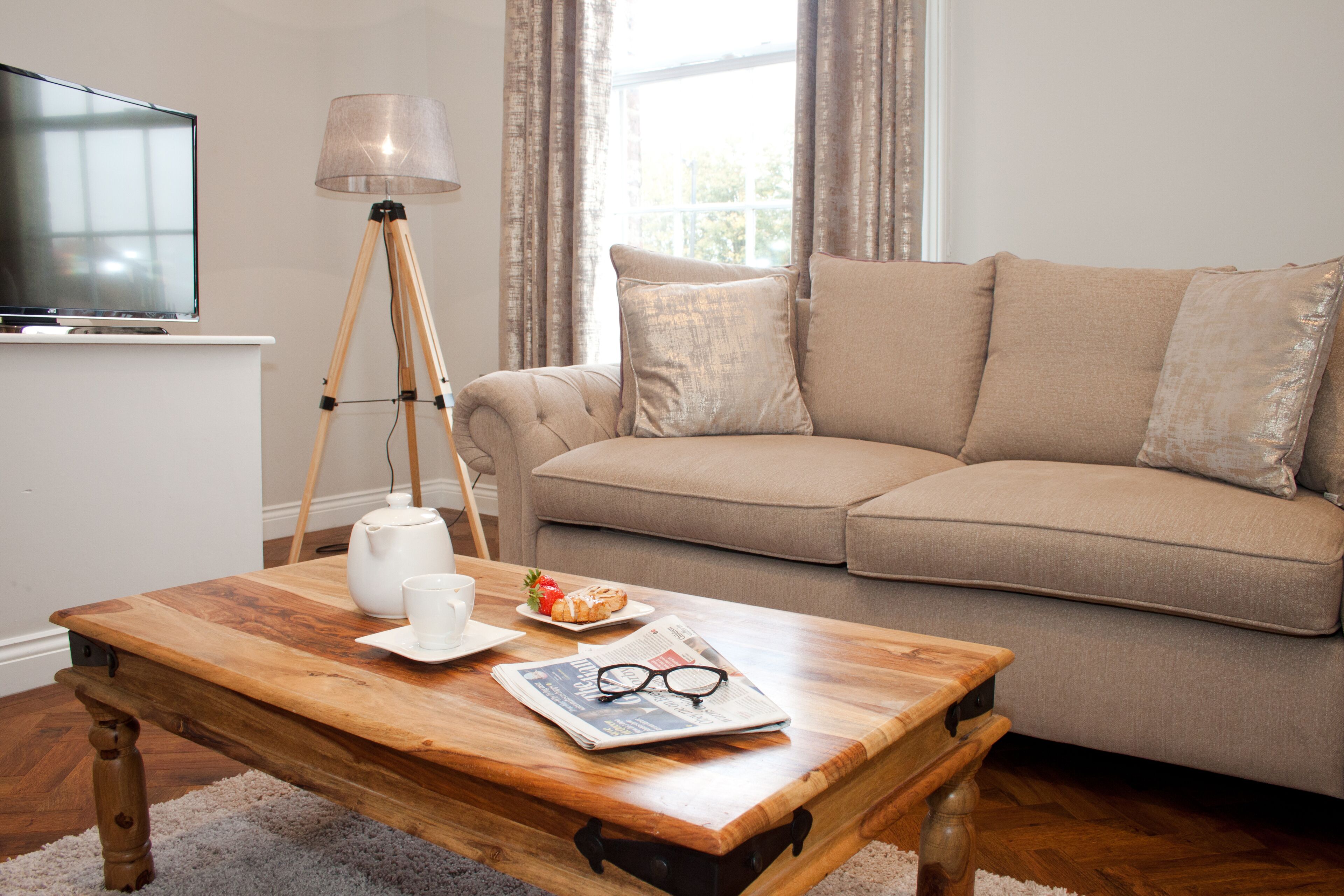 Een woonkamer met een houten salontafel, een bank, een lamp, een televisie en een raam met gordijnen.