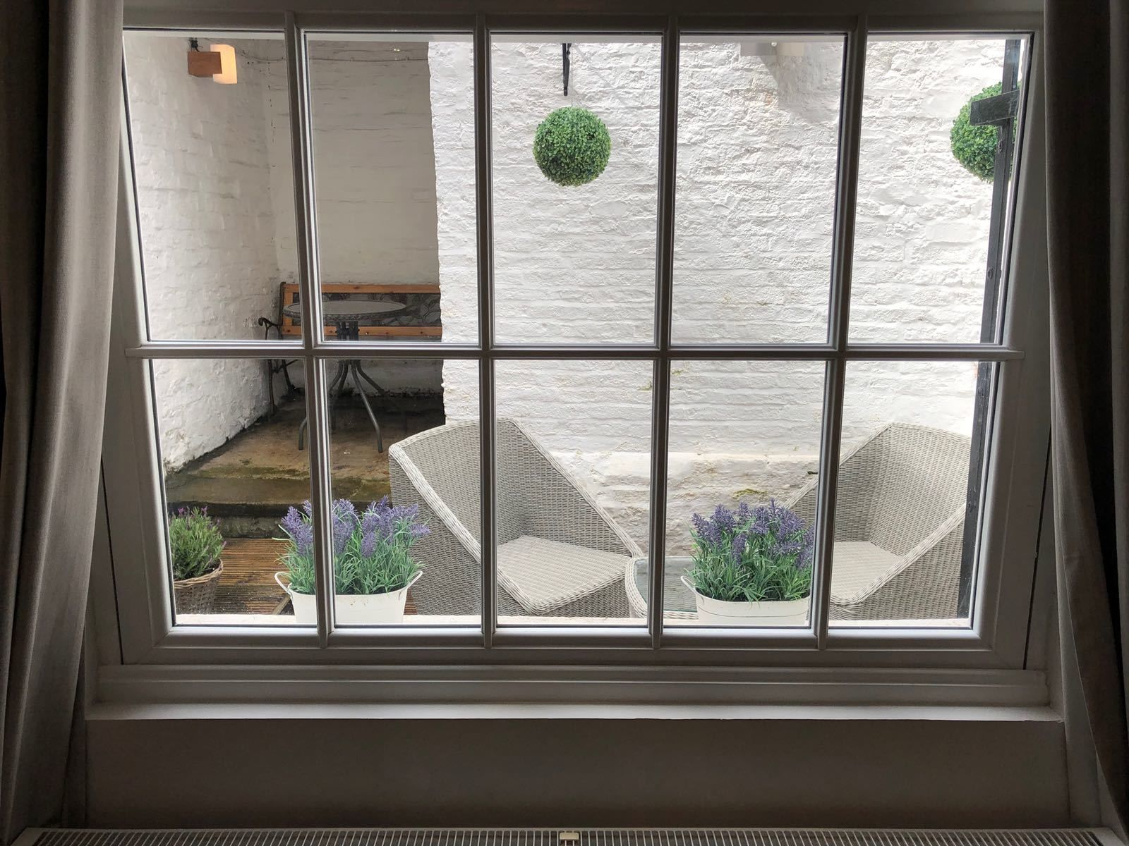A room with a large window divided into nine panes, offering a view of an outdoor patio area with wicker furniture and potted plants.