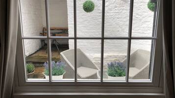 A room with a large window divided into nine panes, offering a view of an outdoor patio area with wicker furniture and potted plants.