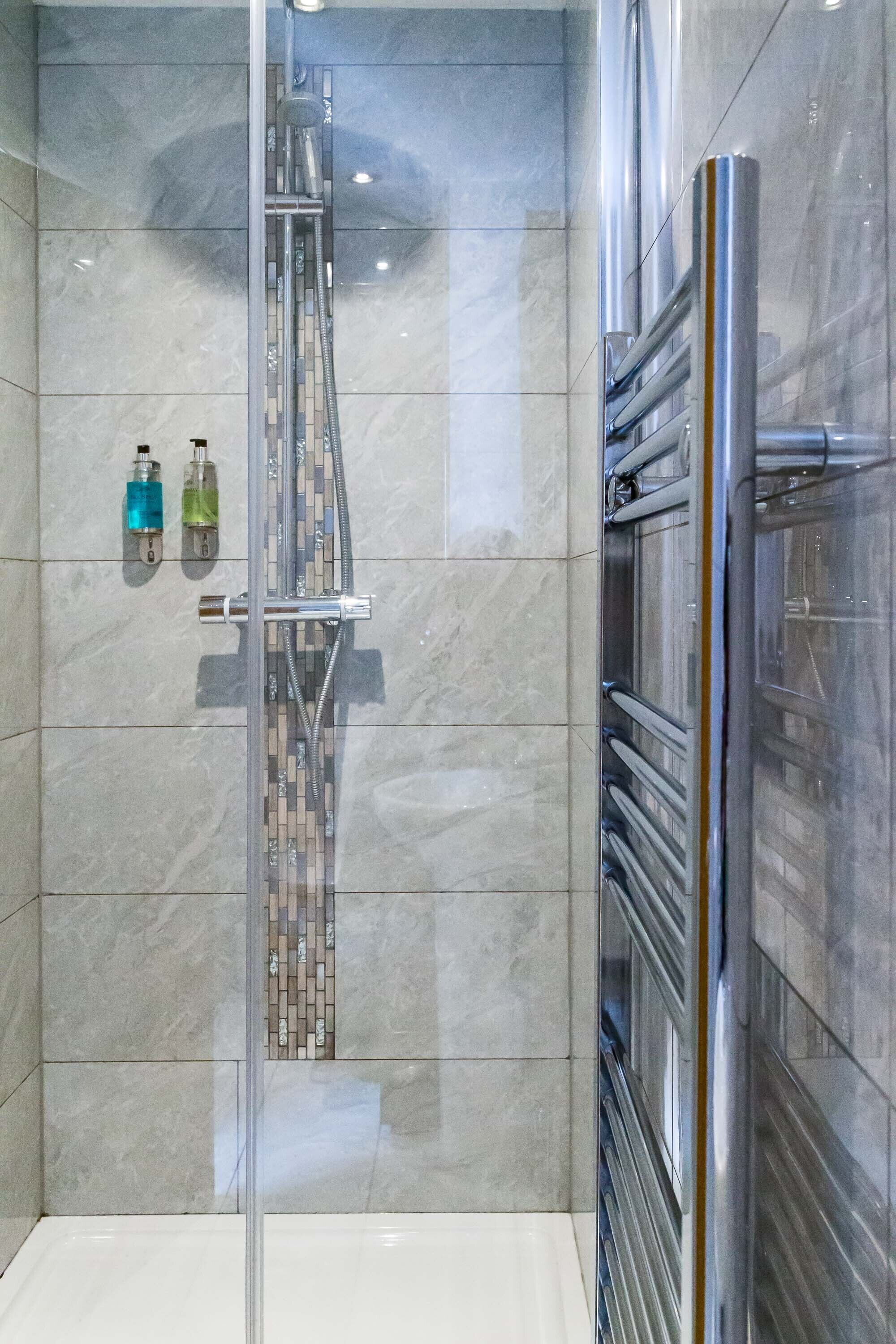 Eine moderne Dusche mit Glastür, Duschkopf aus Chrom und befliester Wand.