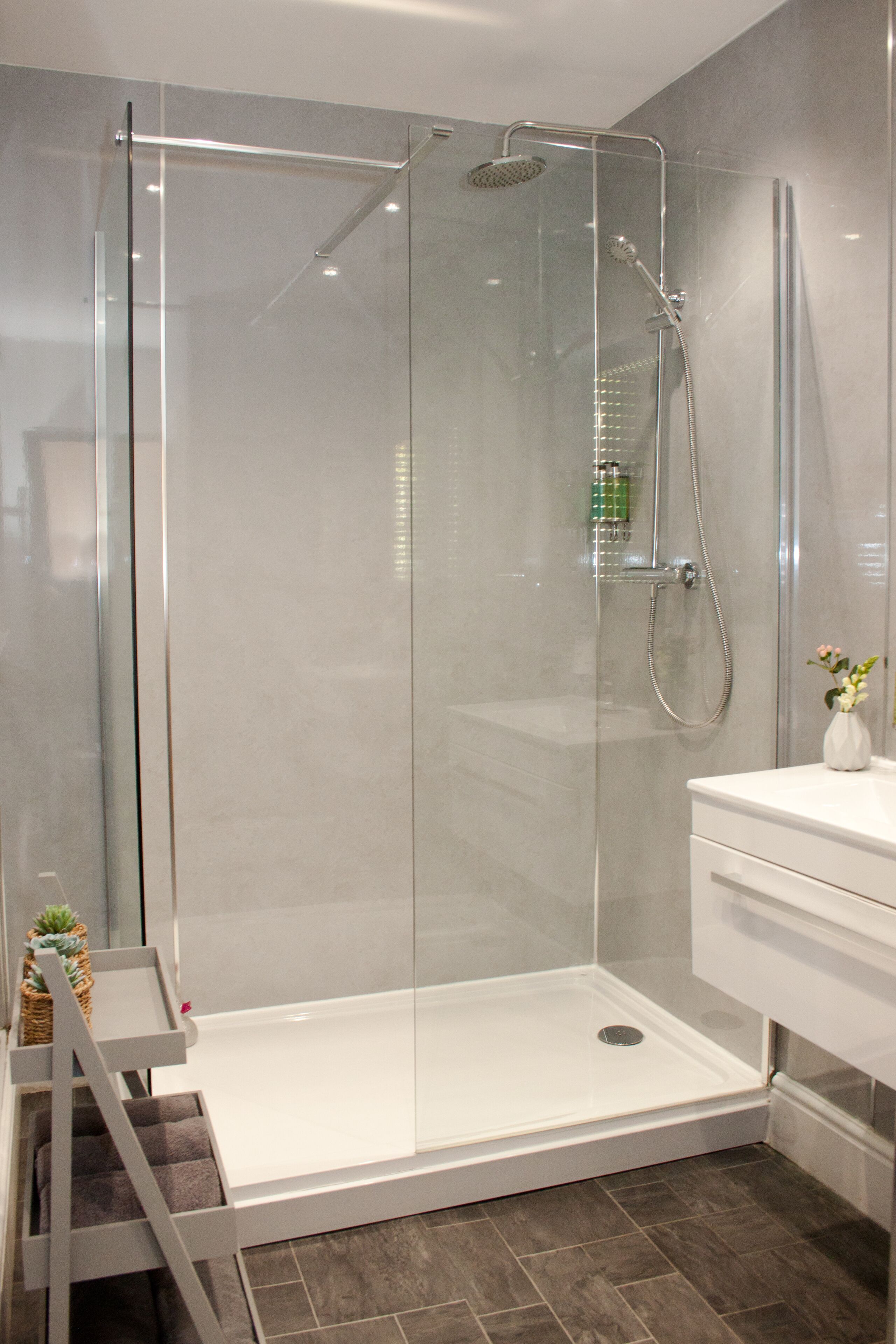 A modern shower enclosure with a glass door, a white sink, and a small potted plant on the counter.