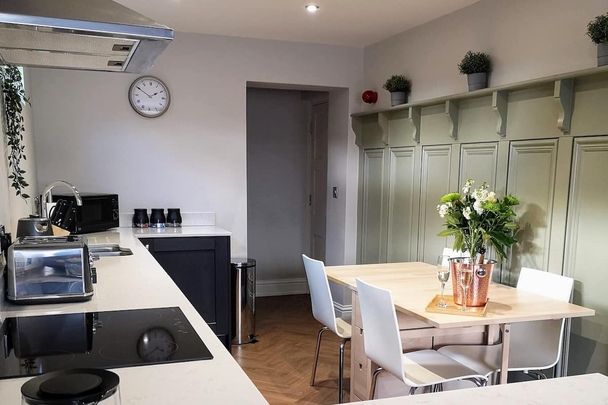 Une cuisine moderne avec un îlot central, un coin repas comprenant une table et des chaises, et une horloge au mur.