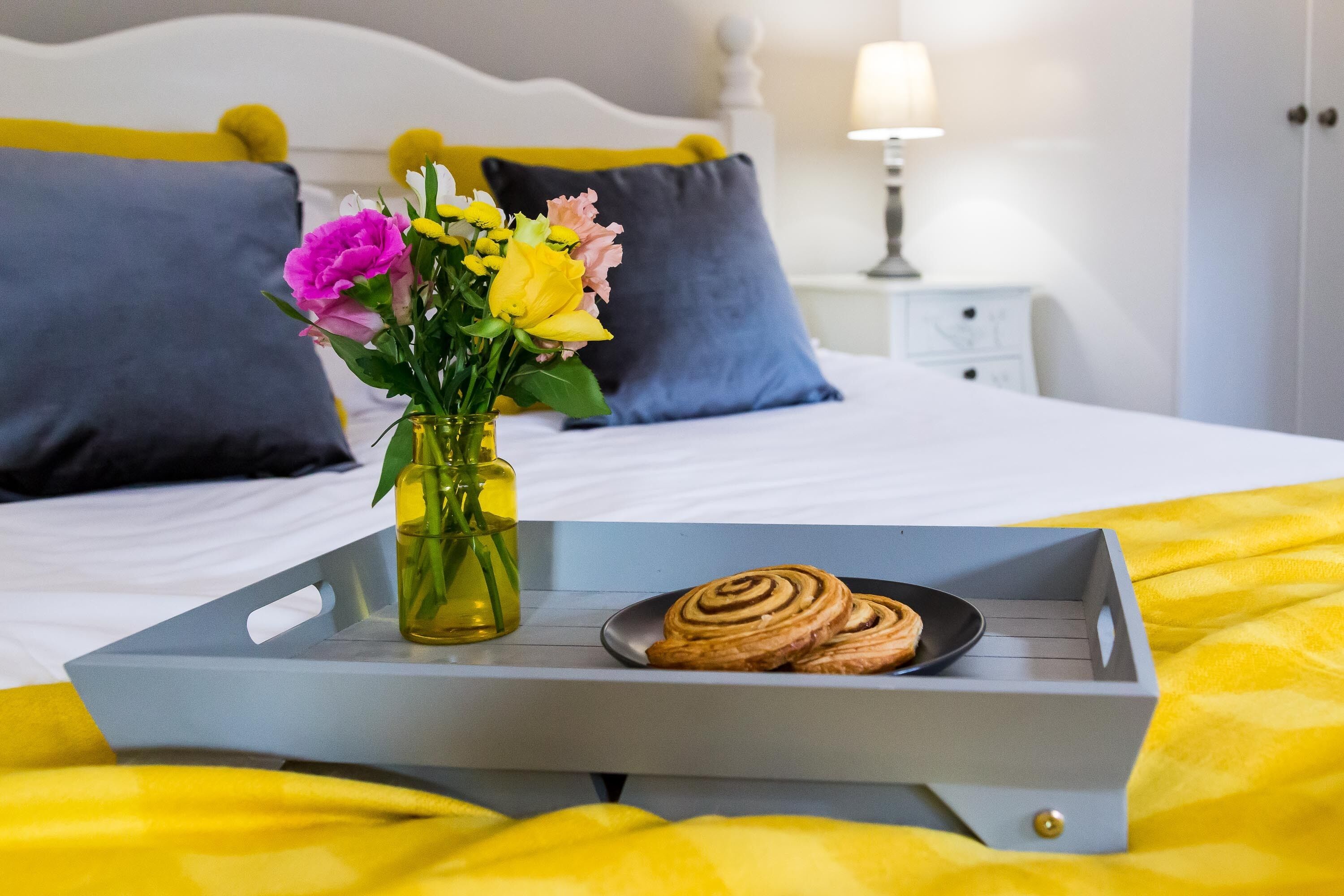 A bed with a tray of pastries and a vase of flowers.