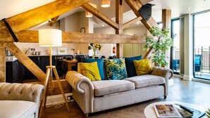 A spacious living room with exposed wooden beams, a sofa with colorful cushions, a lamp, and a dining area in the background. - Goodramgate Apartments (York)