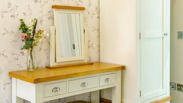 Une coiffeuse blanche avec un miroir, un plateau en bois et des tiroirs, un banc et une armoire blanche avec un plateau en bois.