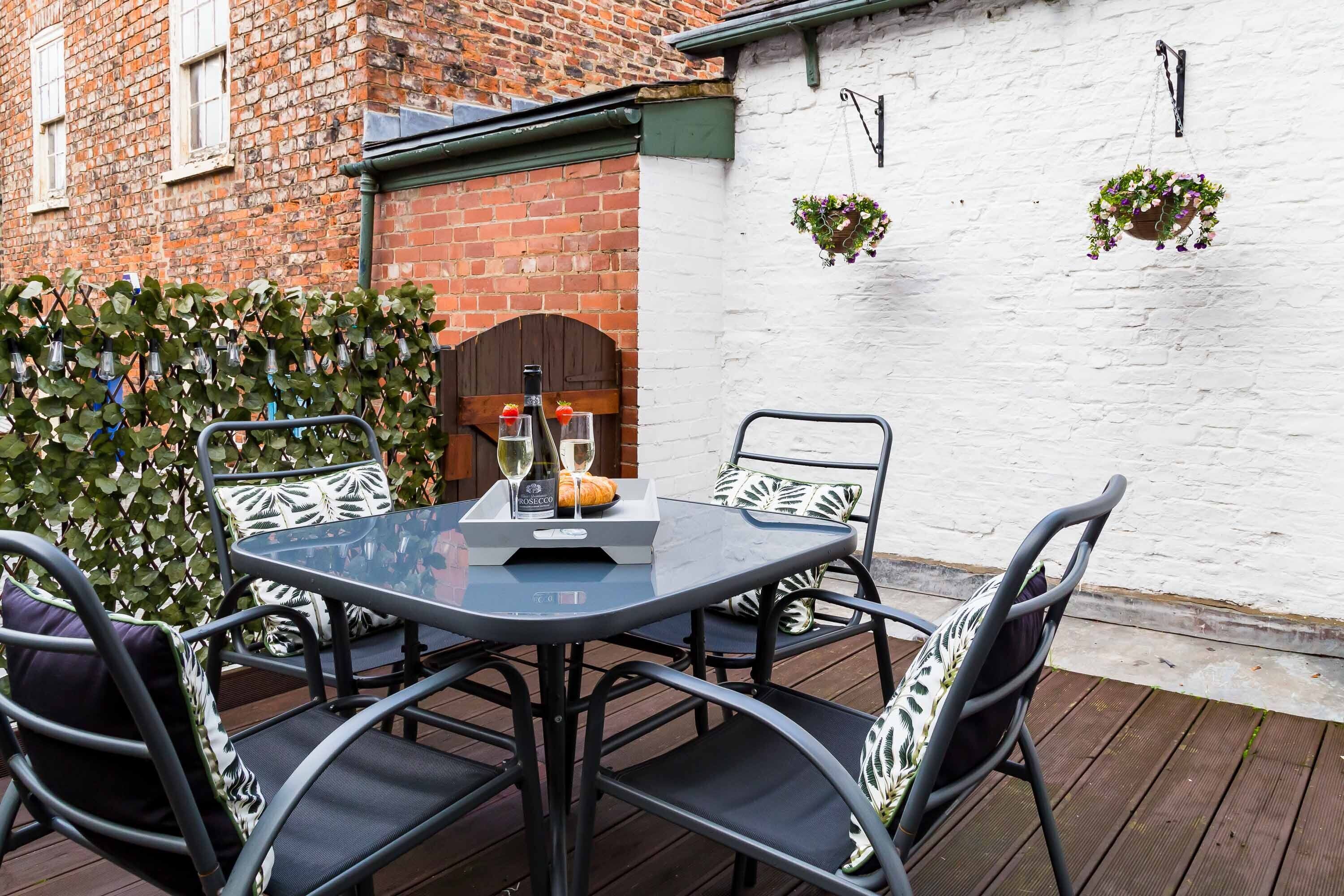 A round table with chairs, a bottle of wine, and a glass on a deck.