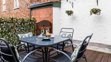 A round table with chairs, a bottle of wine, and a glass on a deck.