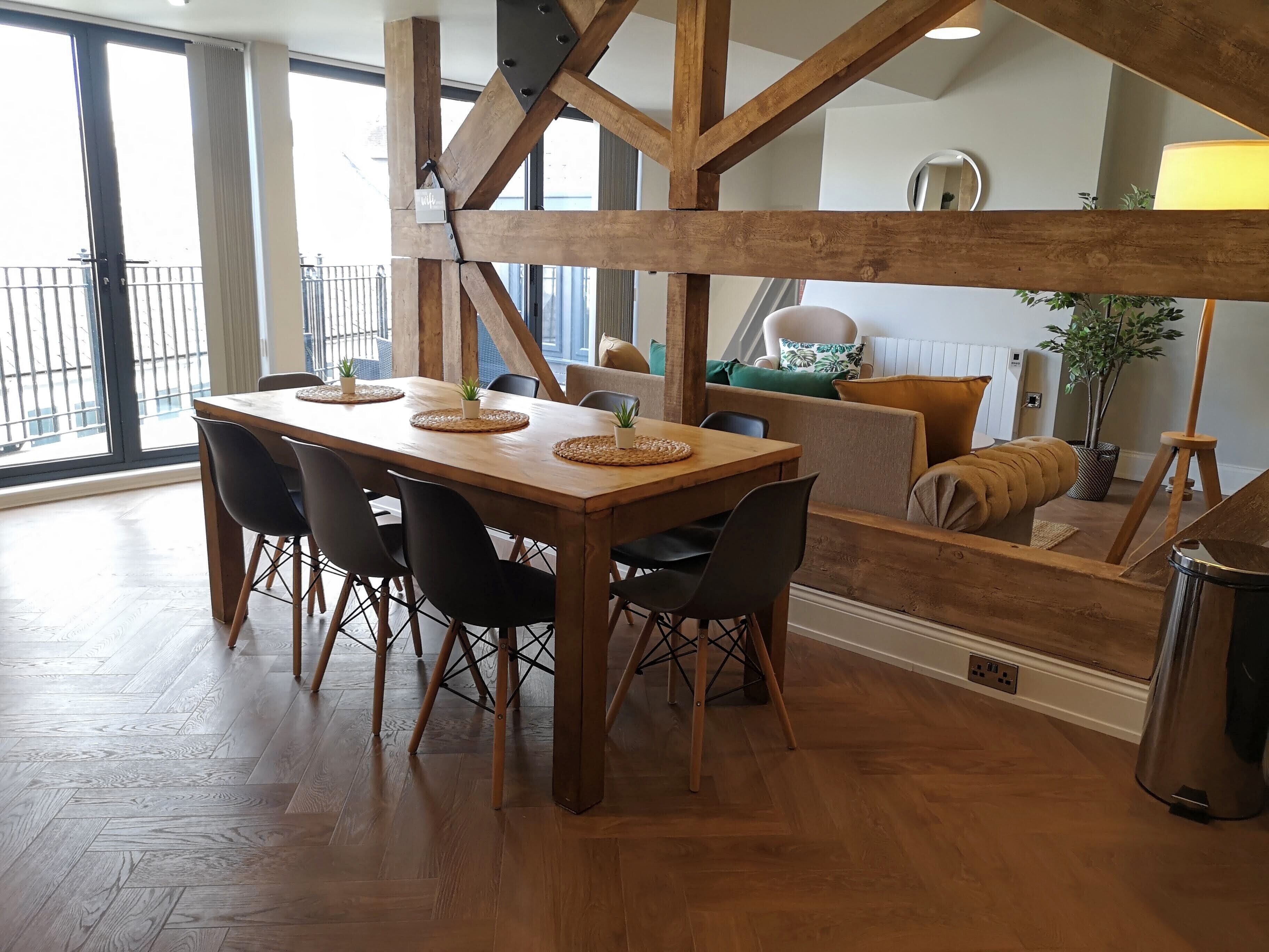 A dining area with a wooden table, black chairs, and a view of the outdoors through large windows.