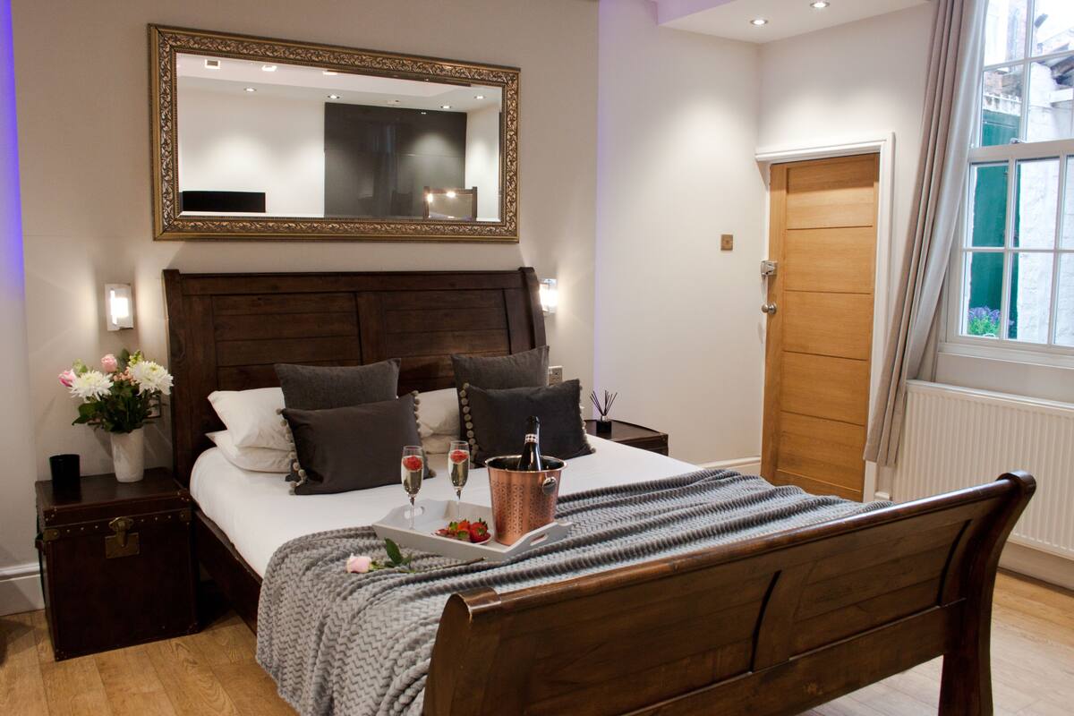 Une chambre à coucher bien rangée, avec un lit en bois, un grand miroir et une fenêtre avec des rideaux.