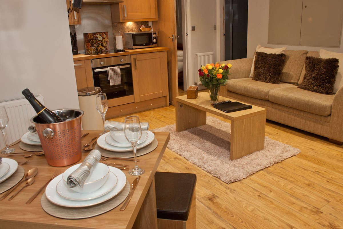 Un coin repas avec une table en bois dressée pour le repas, un seau à vin en cuivre et un vase avec des fleurs posé sur une table basse.