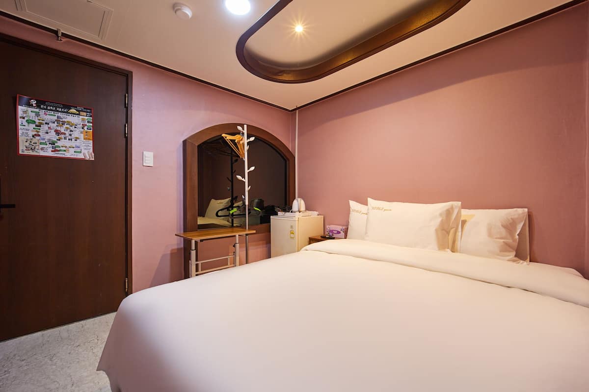 Une chambre d’hôtel équipée d’un lit, d’un bureau, d’un miroir et d’un petit réfrigérateur.