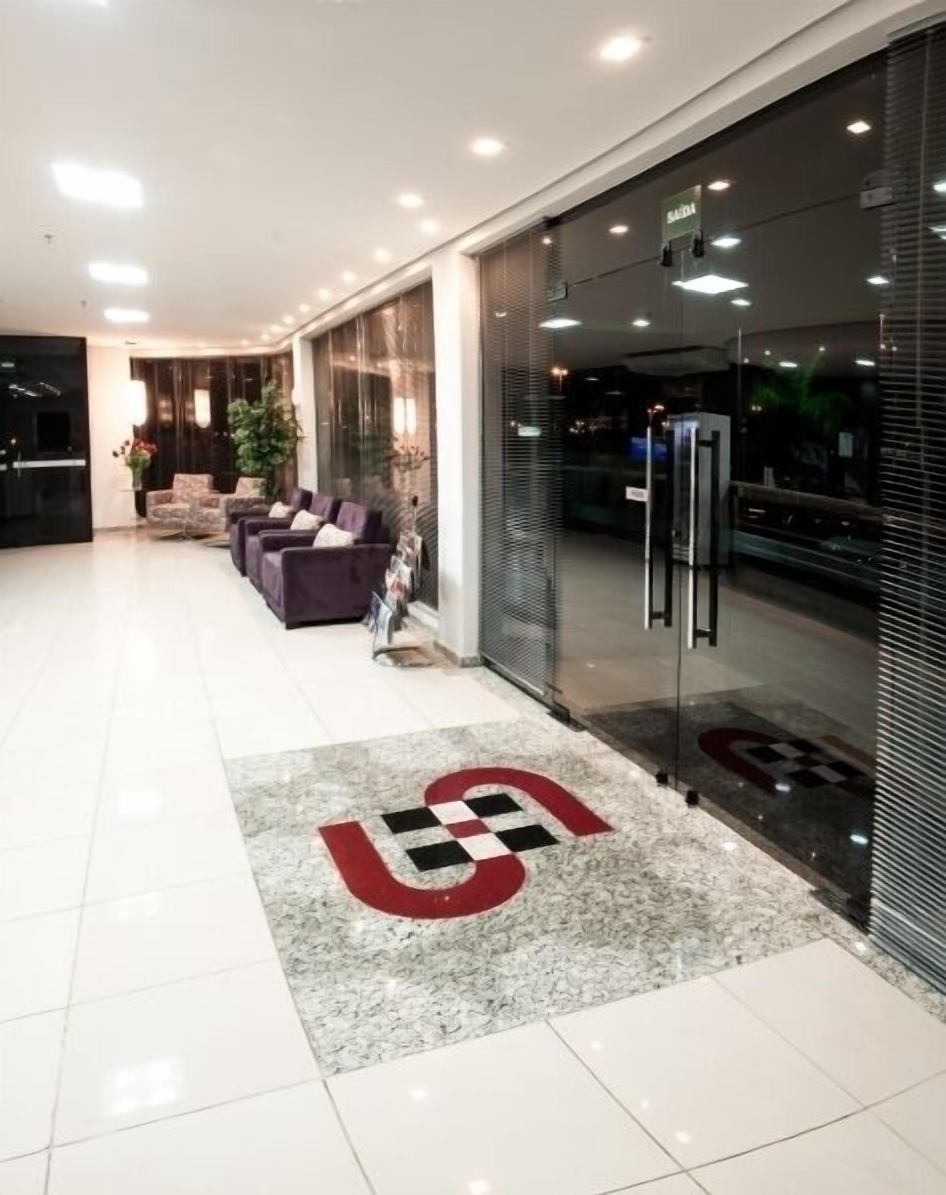A modern hotel lobby with a reception desk, seating area, and a glass wall with a sign.