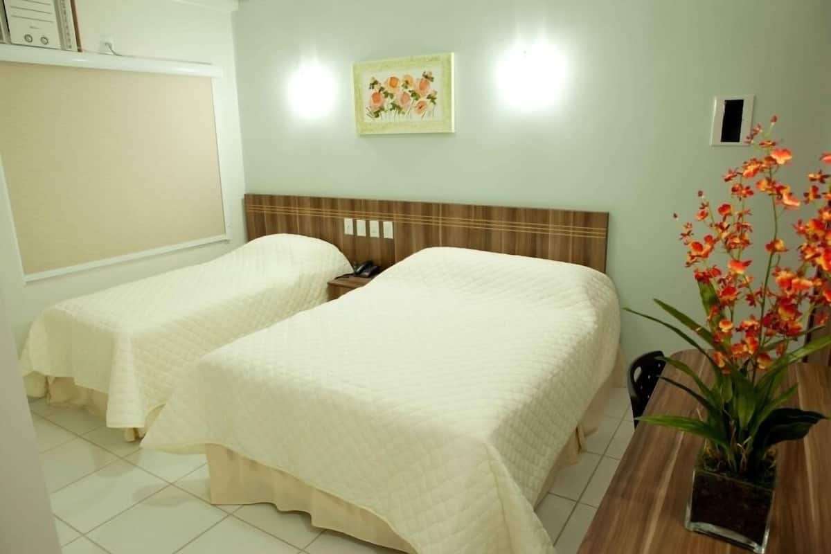 A hotel room with two beds, a wooden nightstand, a small table, and a potted plant.