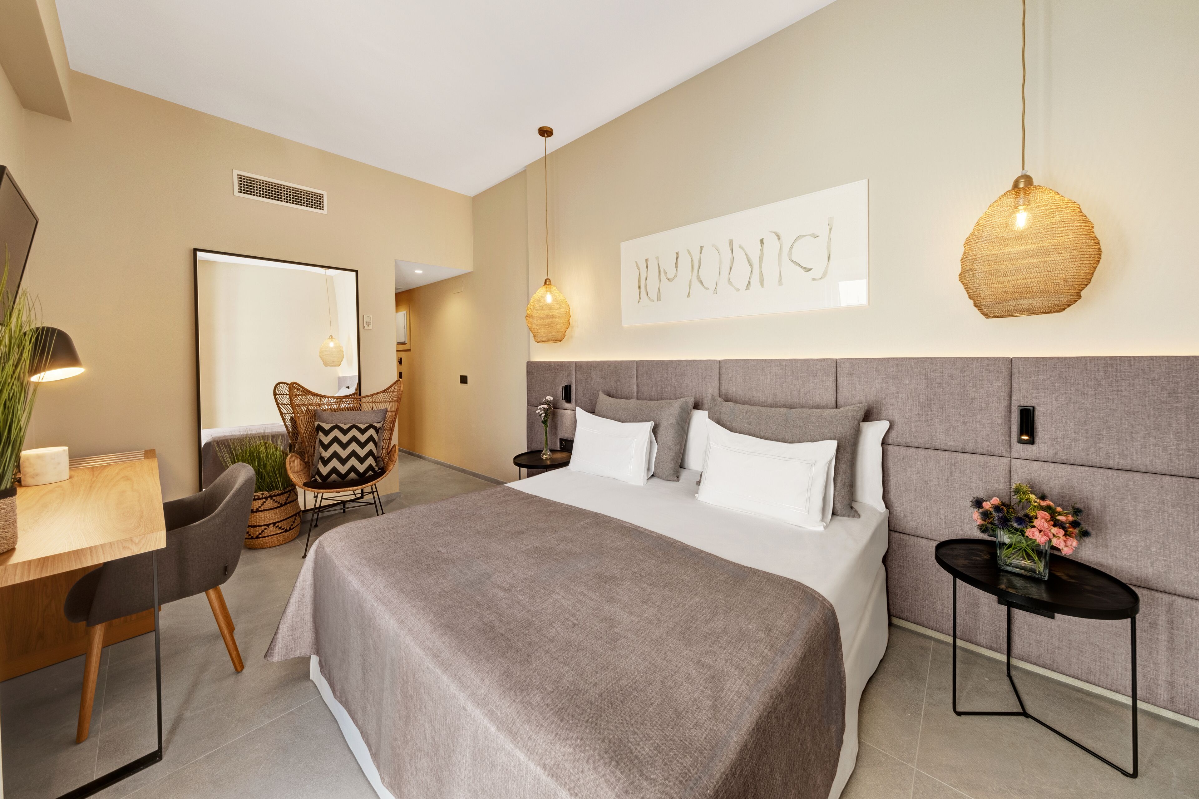 Een moderne hotelkamer met een groot bed, een bureau, een stoel en een kleine tafel met bloemen.