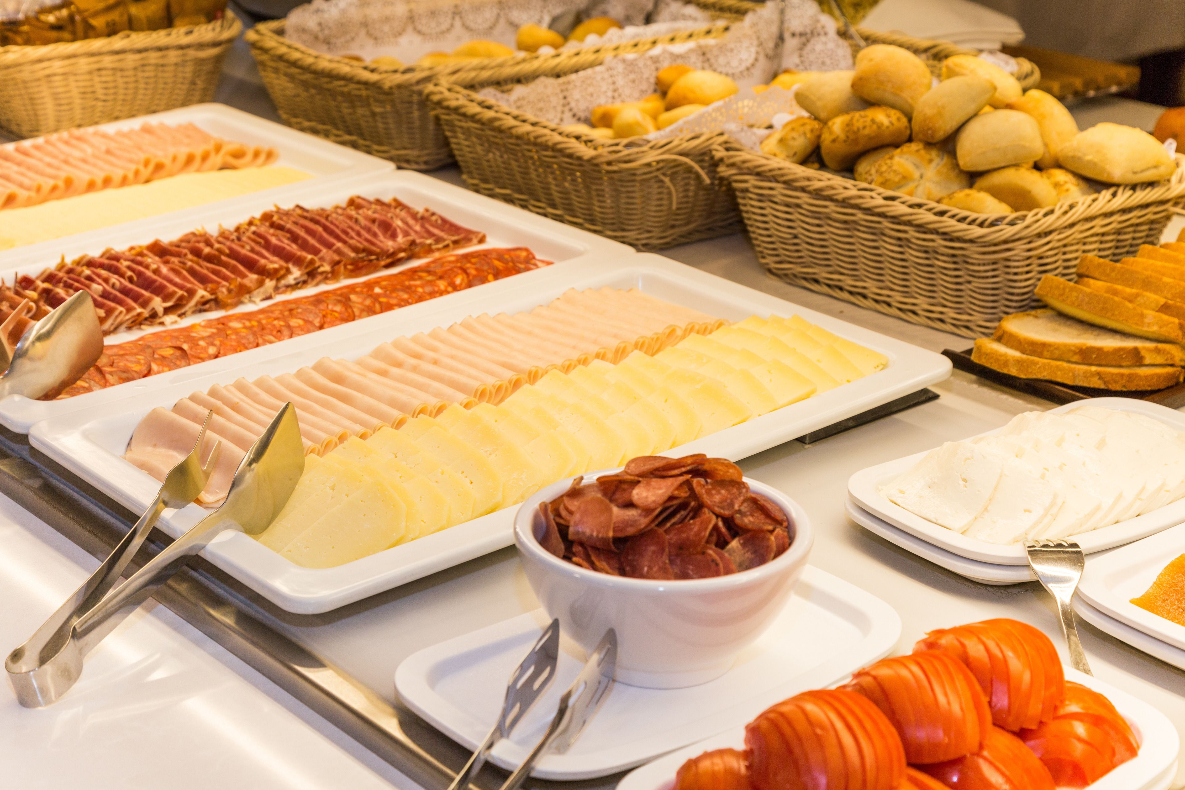 A buffet with various food items including sliced meats, cheeses, and breads.