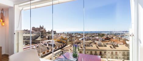 A dining area with a table set for two, overlooking a cityscape with historic buildings and a view of the sea.