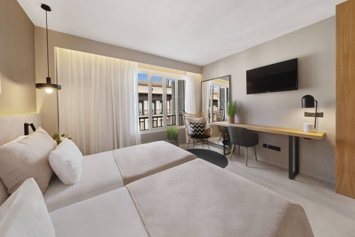 A modern hotel room with a bed, desk, chair, TV, and large windows.