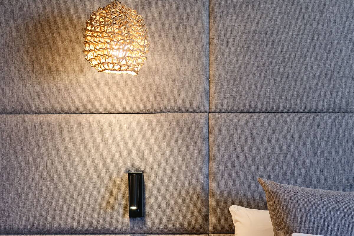 A modern bedroom with a tufted headboard, a bedside table with a plant, and a pendant light.