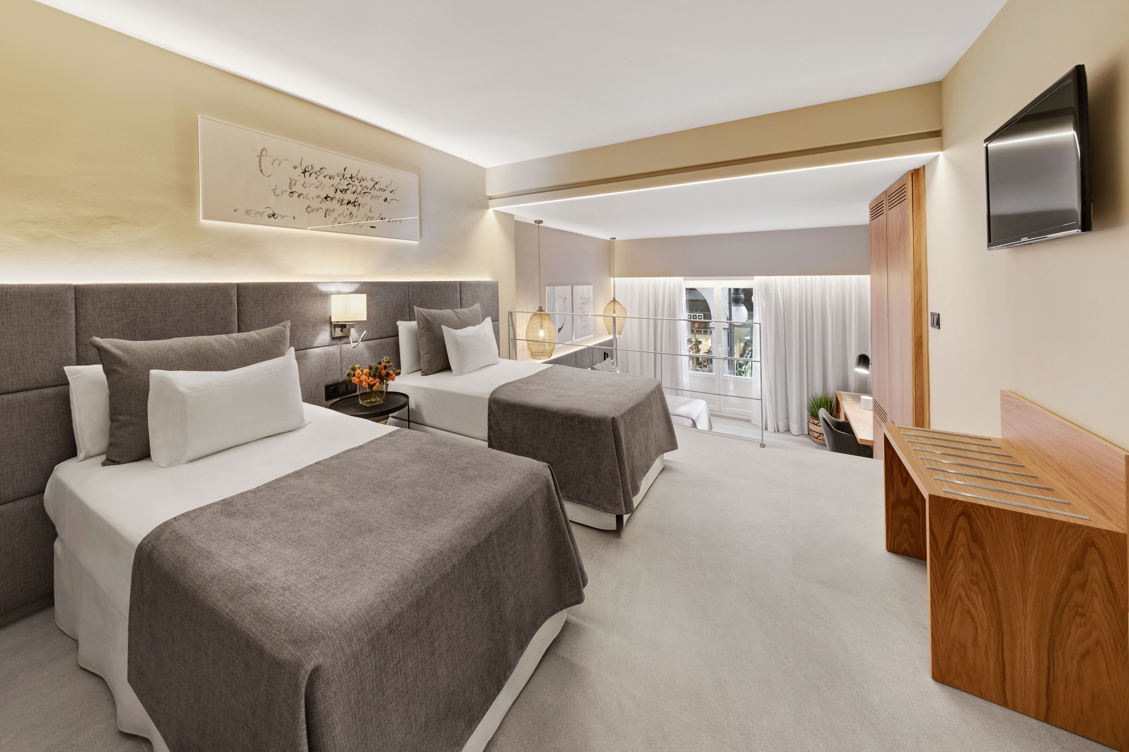 A hotel room with two beds, a TV, a desk, and a balcony with a view.