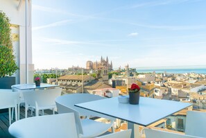 A terrace with white chairs and tables, overlooking a cityscape with historic buildings and a cathedral. - Hotel Almudaina (Palma de Mallorca)