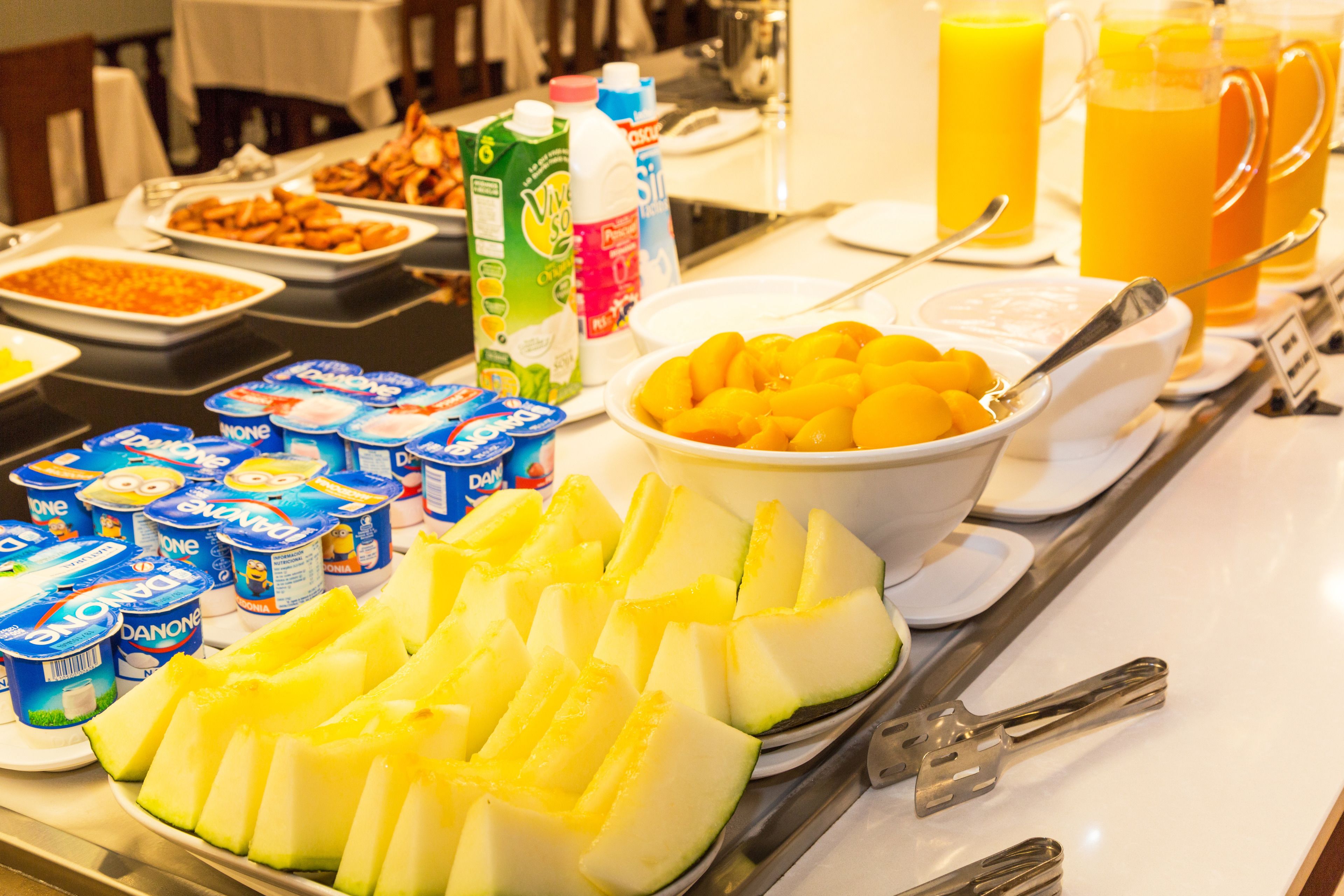 Une table de buffet proposant divers aliments, notamment des fruits, des yaourts et des jus de fruits.