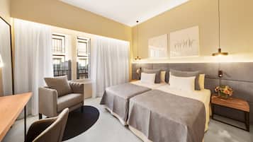 Une chambre d’hôtel avec deux lits, un bureau, une chaise, une table de chevet avec un vase et une fenêtre avec des rideaux.