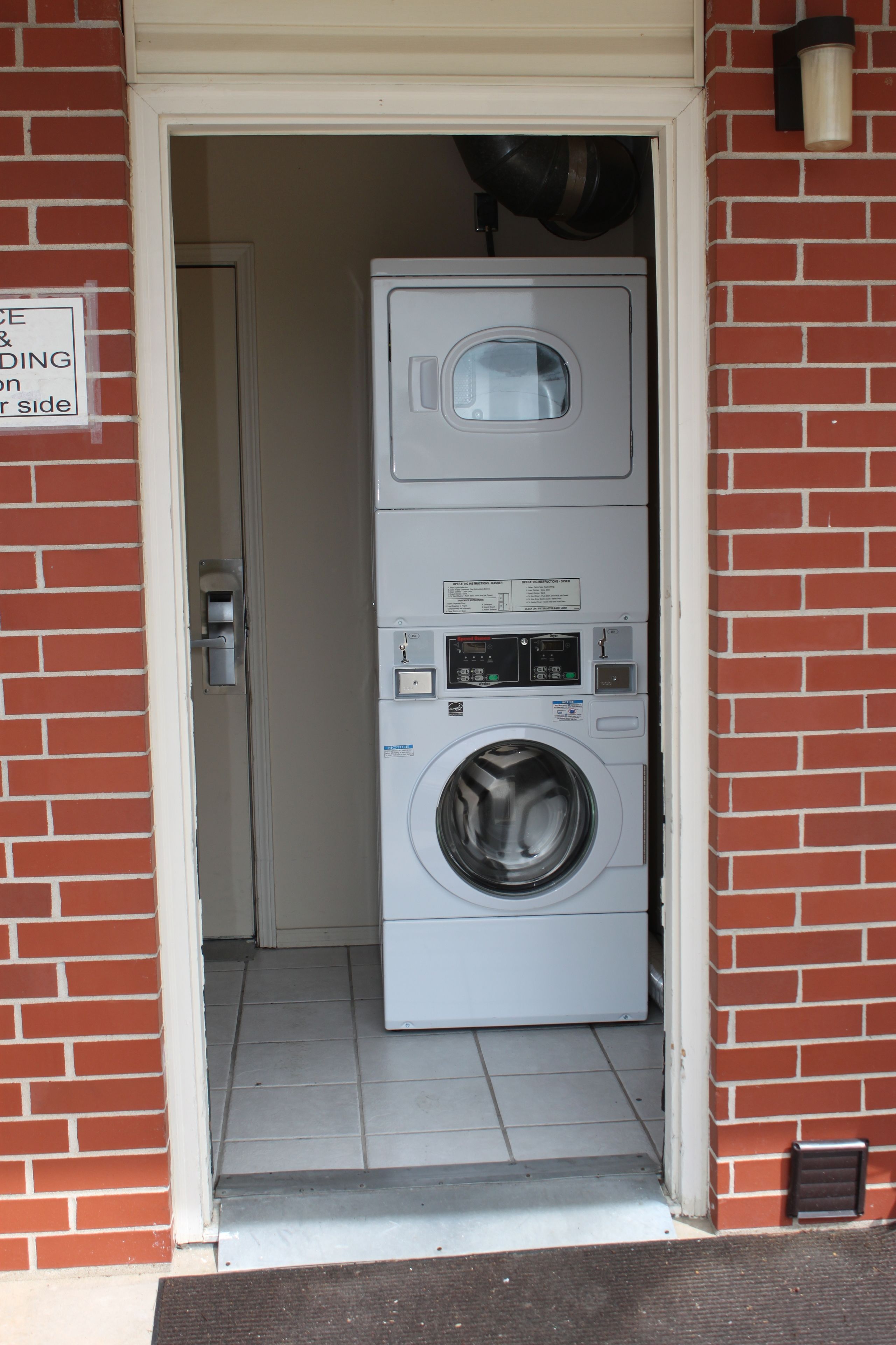 A laundry room with stacked washers and dryers, a door with a sign, and a brick wall.