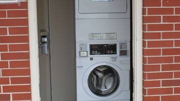 A laundry room with stacked washers and dryers, a door with a sign, and a brick wall.