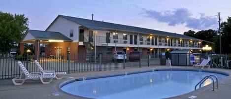 A motel with a swimming pool, a covered area, and a fenced parking lot.