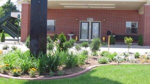 Un edificio de ladrillo con un porche cubierto, un buzón y un pequeño jardín con diversas plantas y flores.