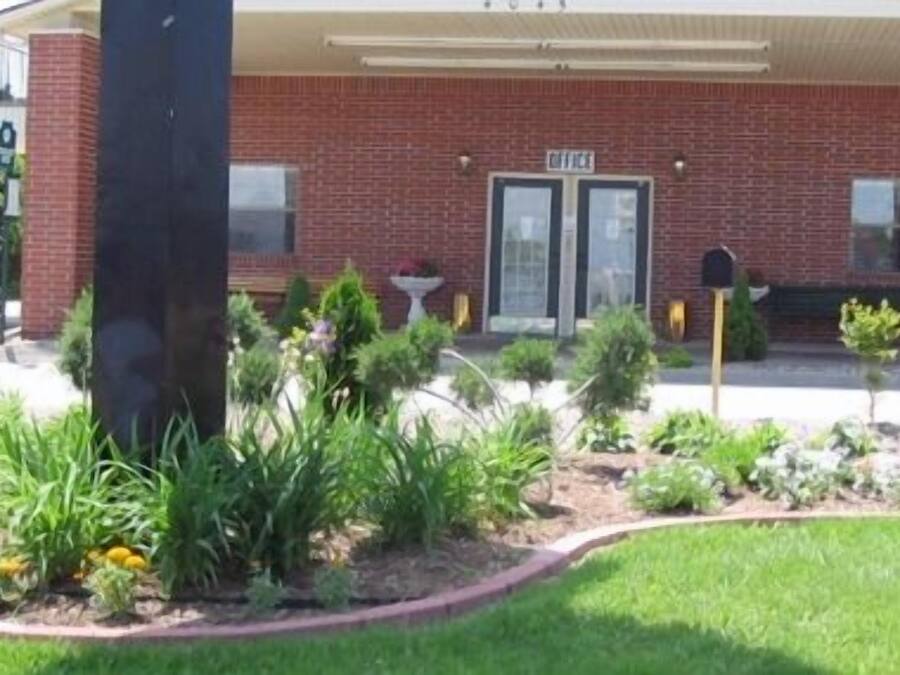 A brick building with a covered entrance, a mailbox, and a small garden area with various plants and flowers.