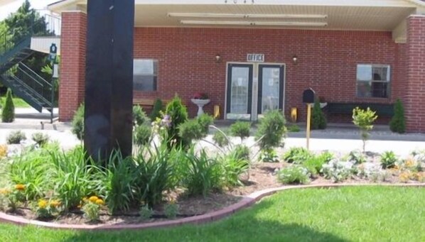 A brick building with a covered entrance, a mailbox, and a small garden area with various plants and flowers.